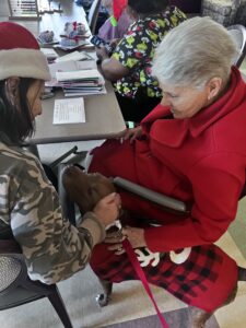 two older women sitting, petting a dog in a holiday sweater